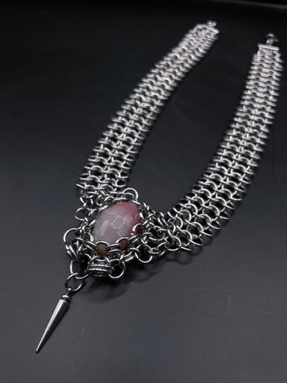 Silver chain necklace with a pink stone and spike pendant on a dark background