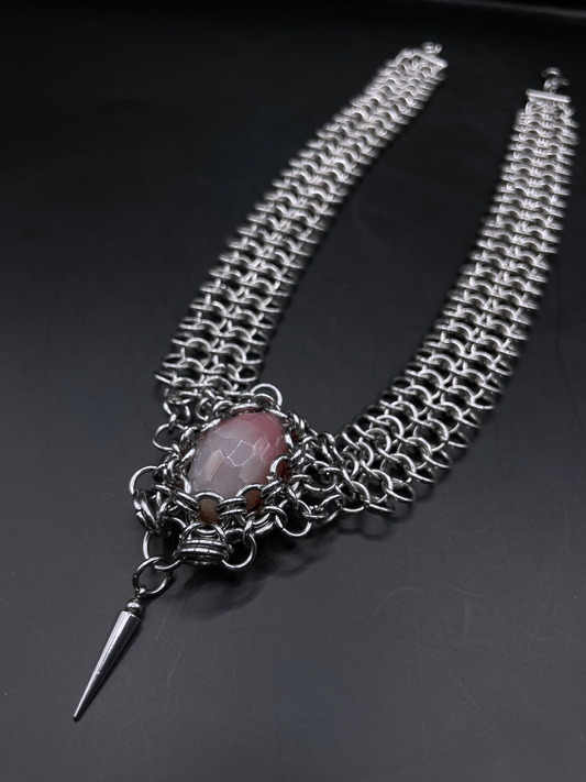 Silver chain necklace with a pink stone and spike pendant on a dark background