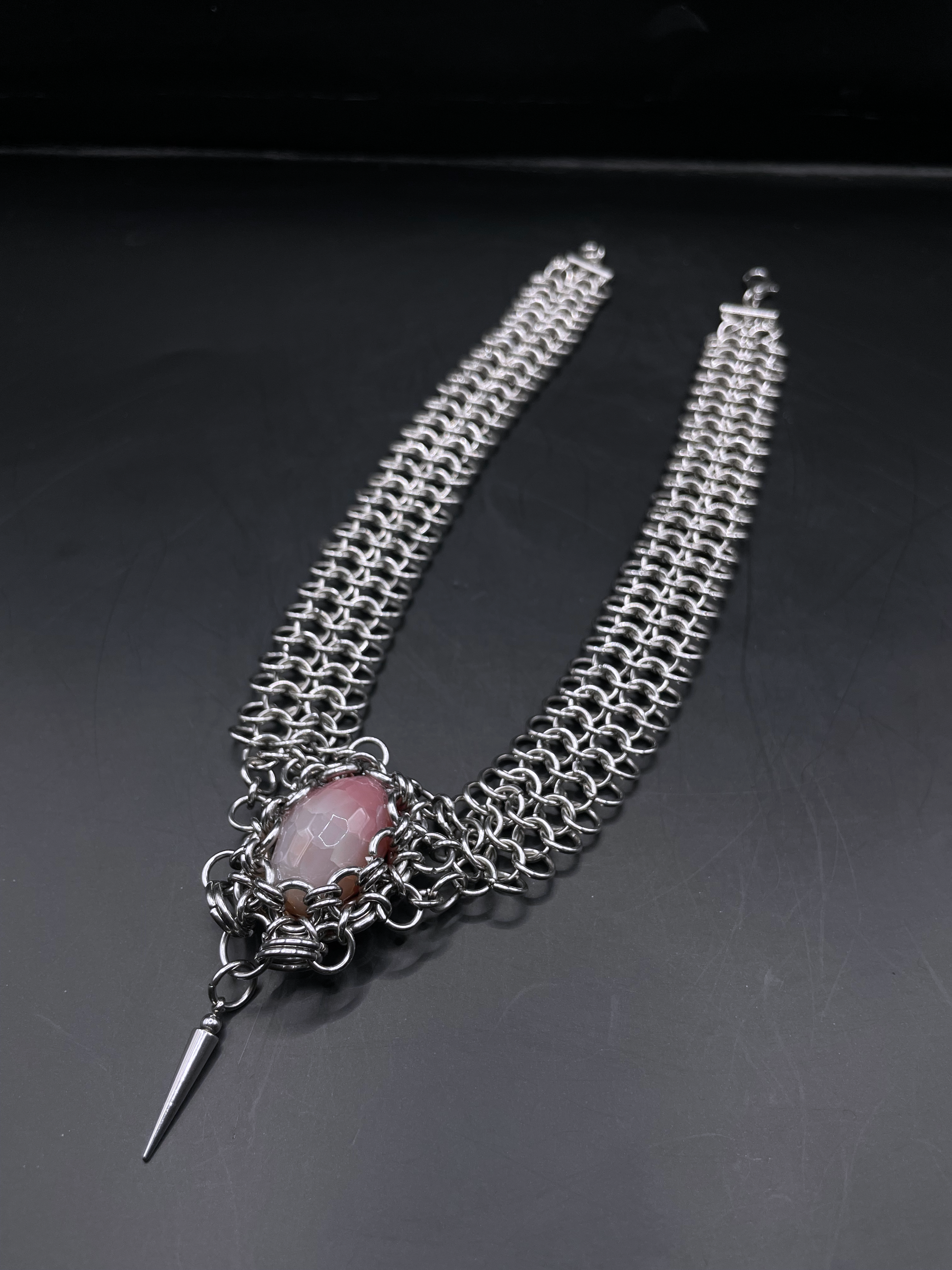 Chainmail necklace with a central pink stone and a spike on a dark background