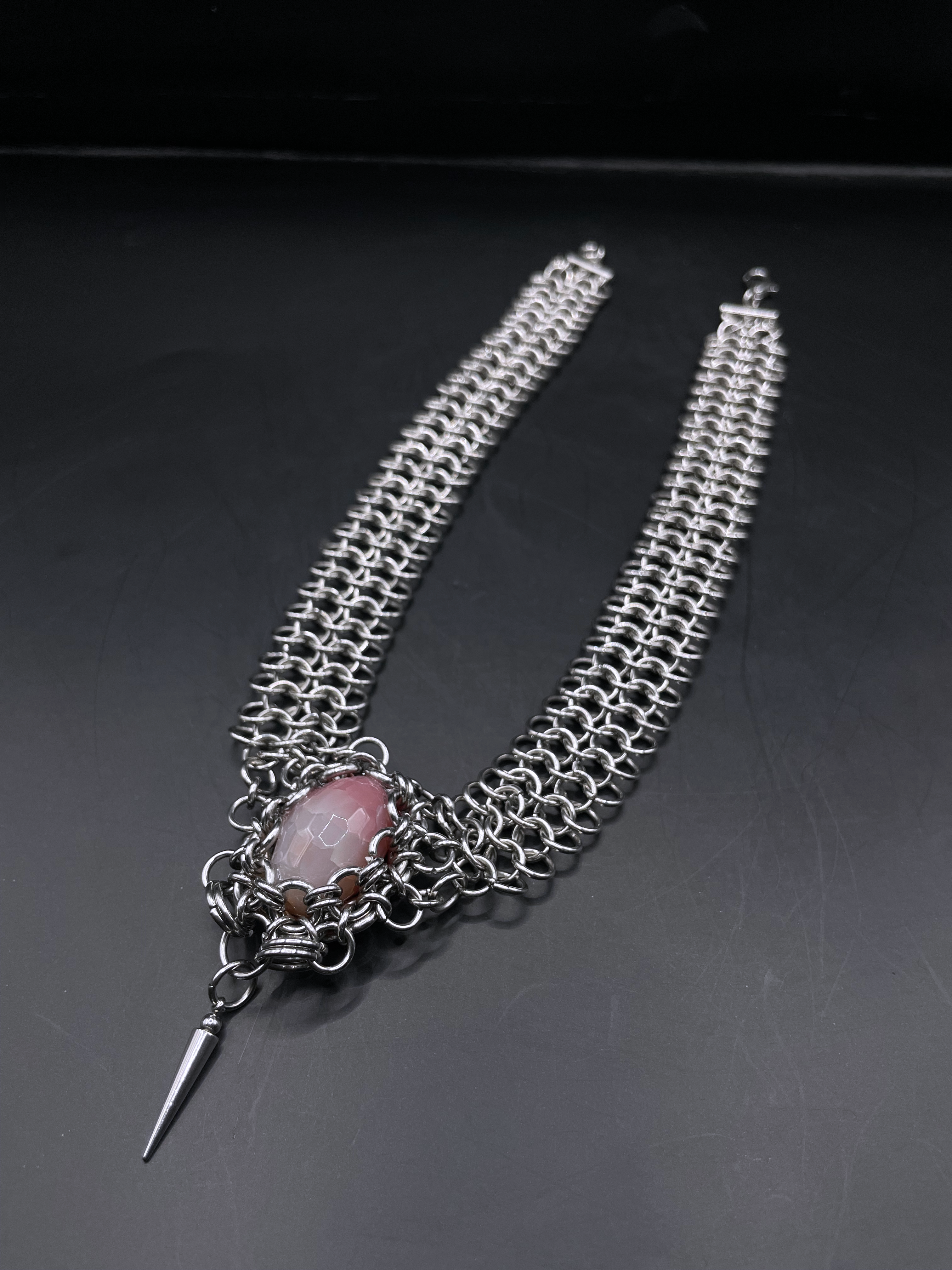 Chainmail necklace with a central pink stone and a spike on a dark background