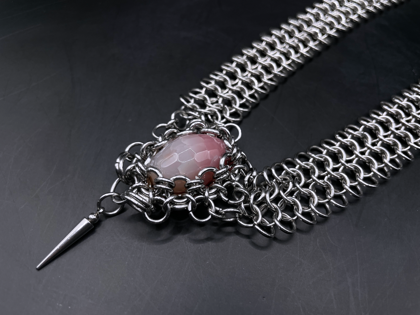Chainmail necklace with a pink stone and spike on a dark background