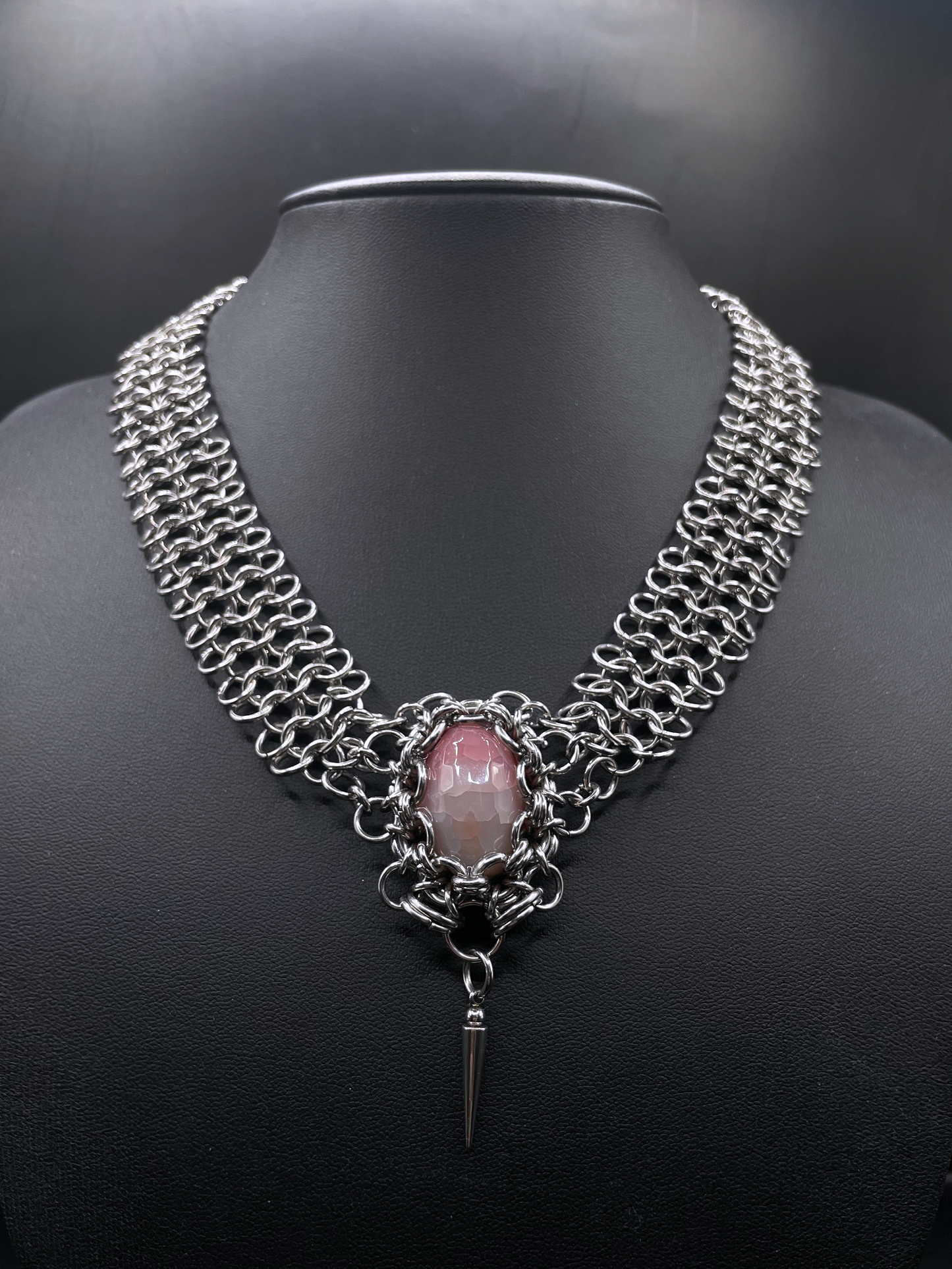 Chainmail necklace with a pink stone and black background