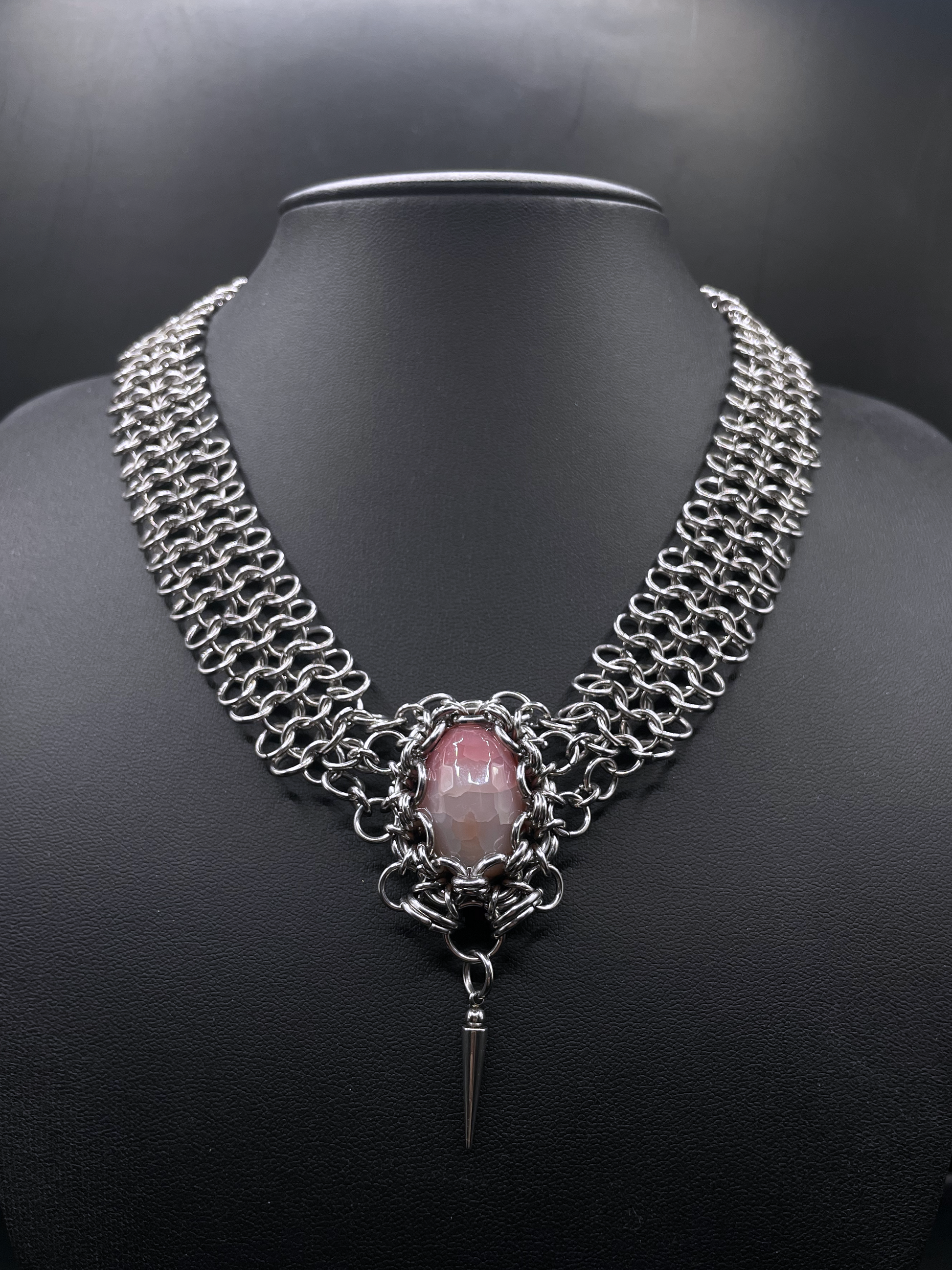 Chainmail necklace with a pink stone and black background