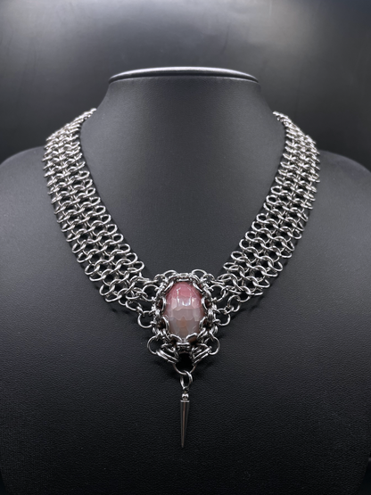 Chainmail necklace with a pink stone and black background