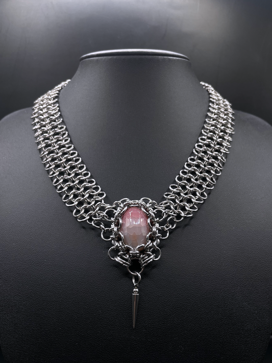 Chainmail necklace with a pink stone and black background