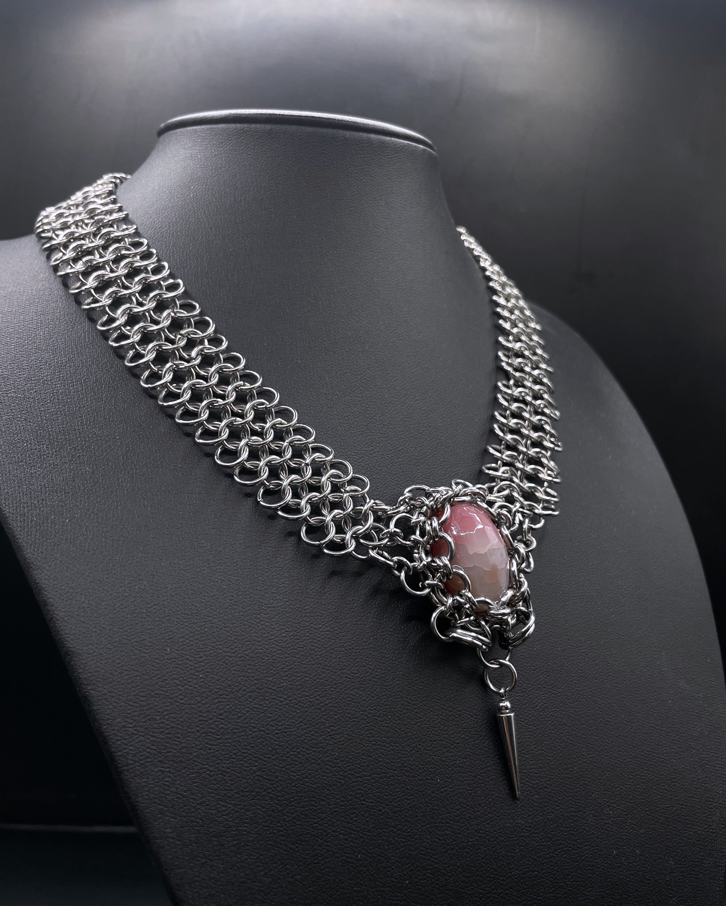 Chainmail necklace with a pink stone and black background